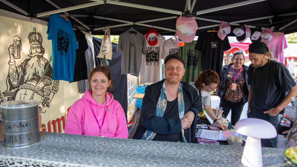 Merch-Stand mit Bandshirts und Besucherinnen an der Theke beim Göss OpenAir 2026 in Gössmannsreuth.