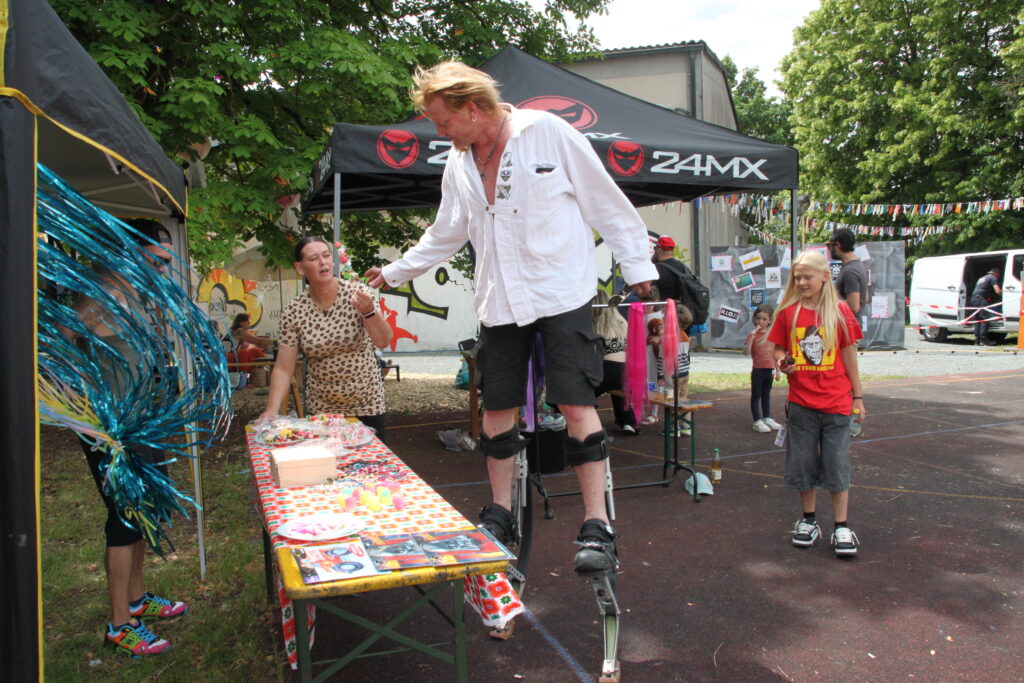 Stelzenläufer unterhält Kinder an einem Bastelstand beim Göss OpenAir 2026 in Gössmannsreuth.