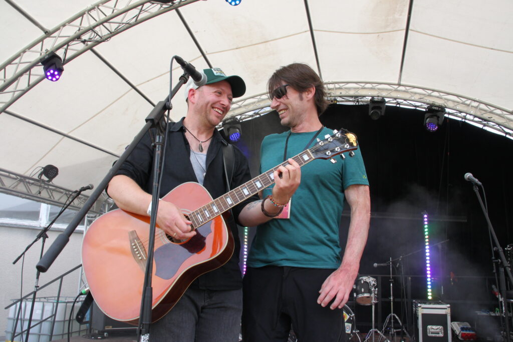 Zwei Musiker lachen gemeinsam mit Gitarre auf der Bühne beim Göss OpenAir 2026 in Gössmannsreuth.